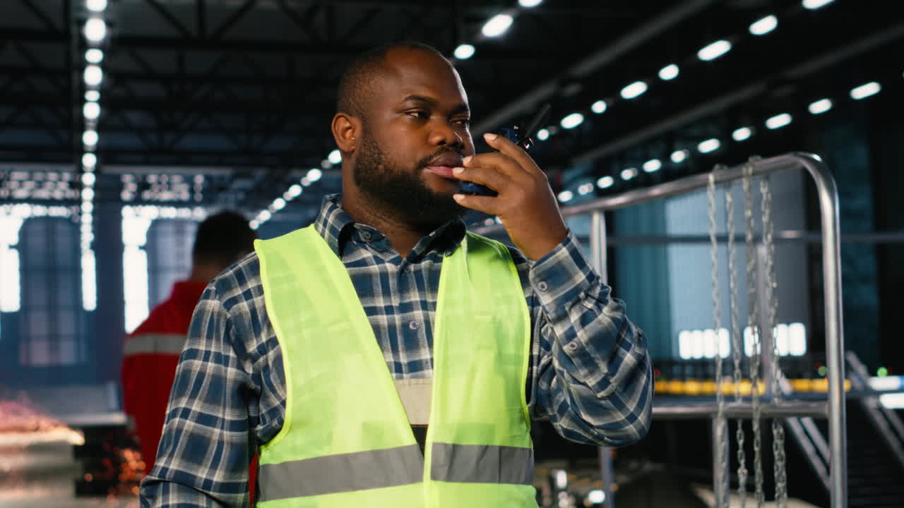Black manufacturing employee uses walkie talkie to speak with supervisor