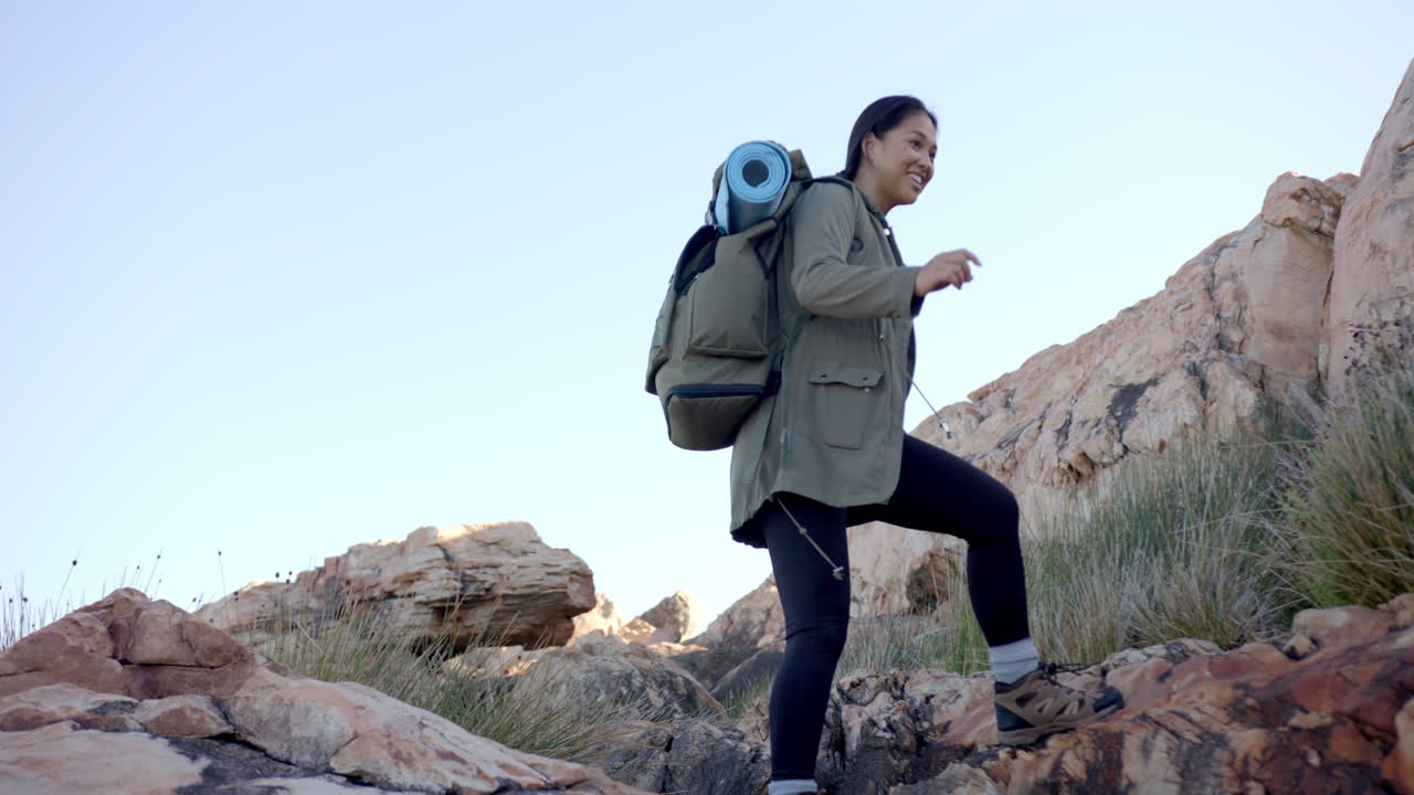 Hiking in mountains, woman with backpack and yoga mat navigating rocky terrain