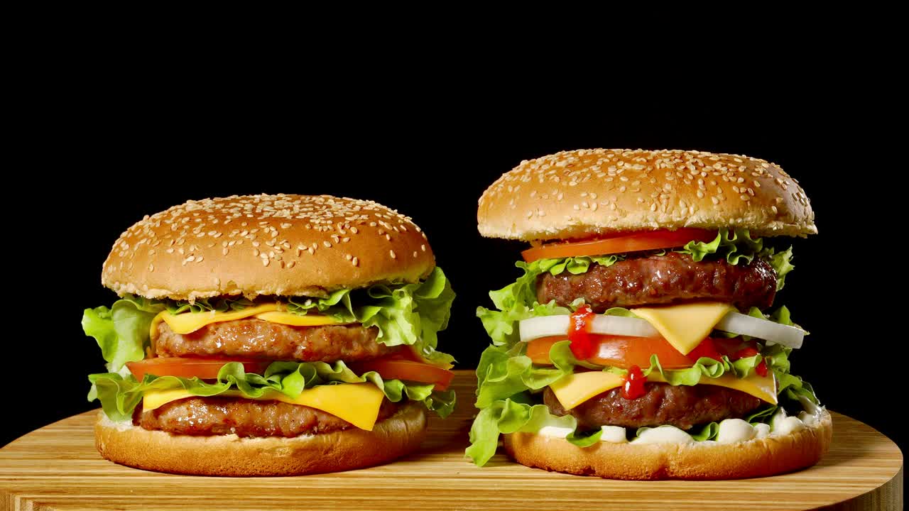 primer plano de dos hamburguesas apetitosas con panes de sésamo girando sobre un fondo negro, de comida rápida en bucle sin costuras
