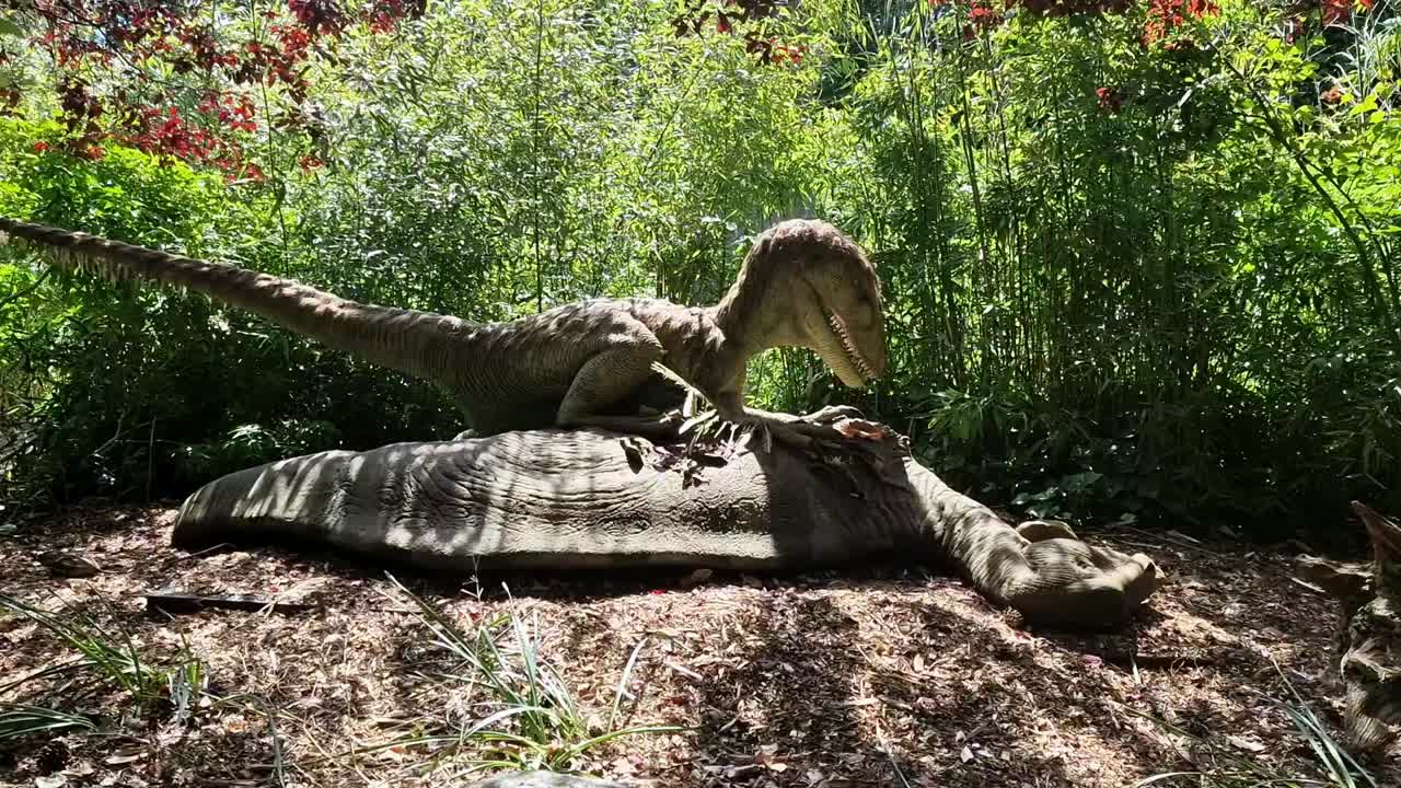Animated robot raptor dinosaur standing over it's prey in dense woodland forest theme park attraction