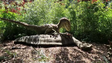 Animated robot raptor dinosaur standing over it&#039;s prey in dense woodland forest theme park attraction