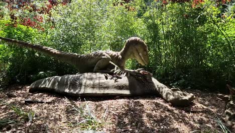 animated robot raptor dinosaur standing over it's prey in dense woodland forest theme park attraction