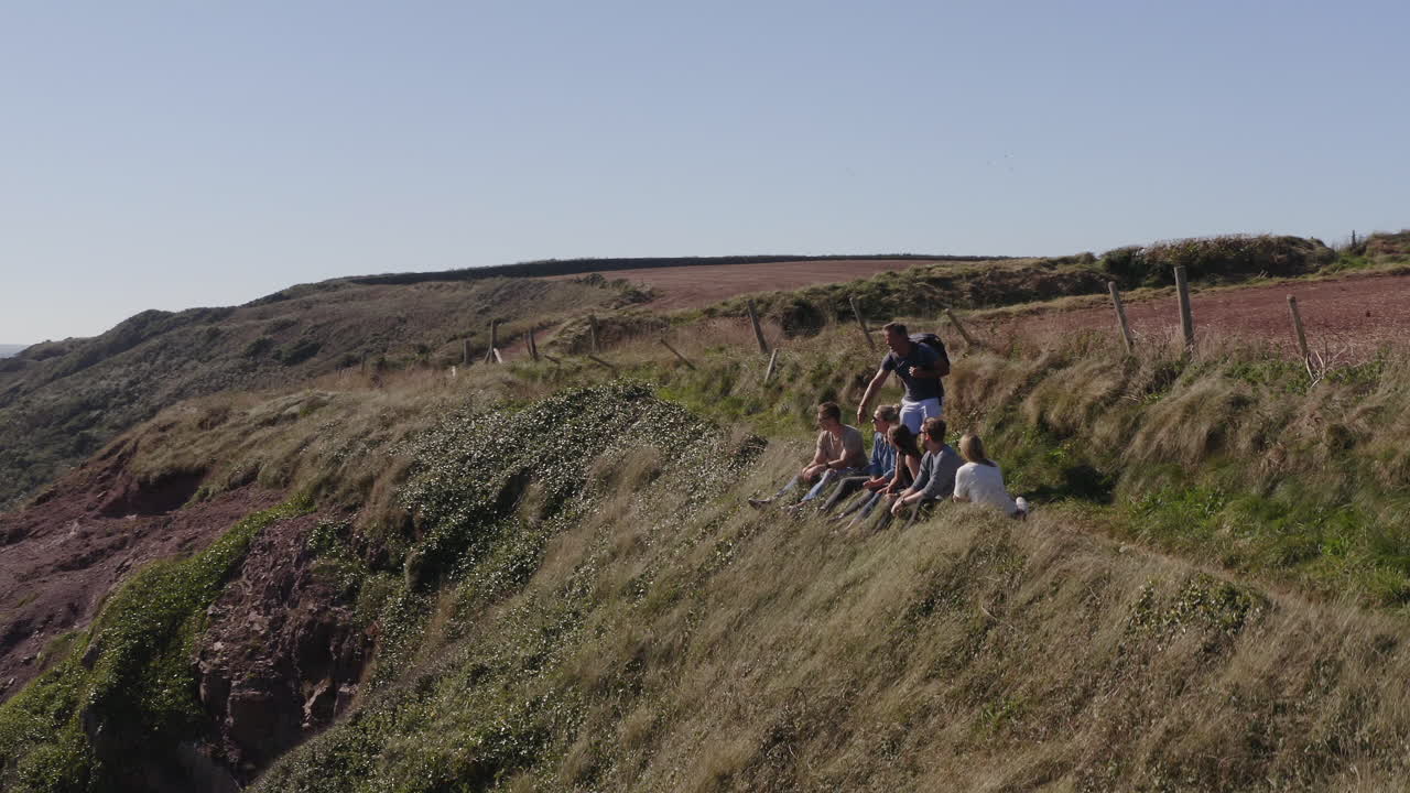 Ripresa con drone di un gruppo di amici che fanno trekking lungo le scogliere su un sentiero costiero.