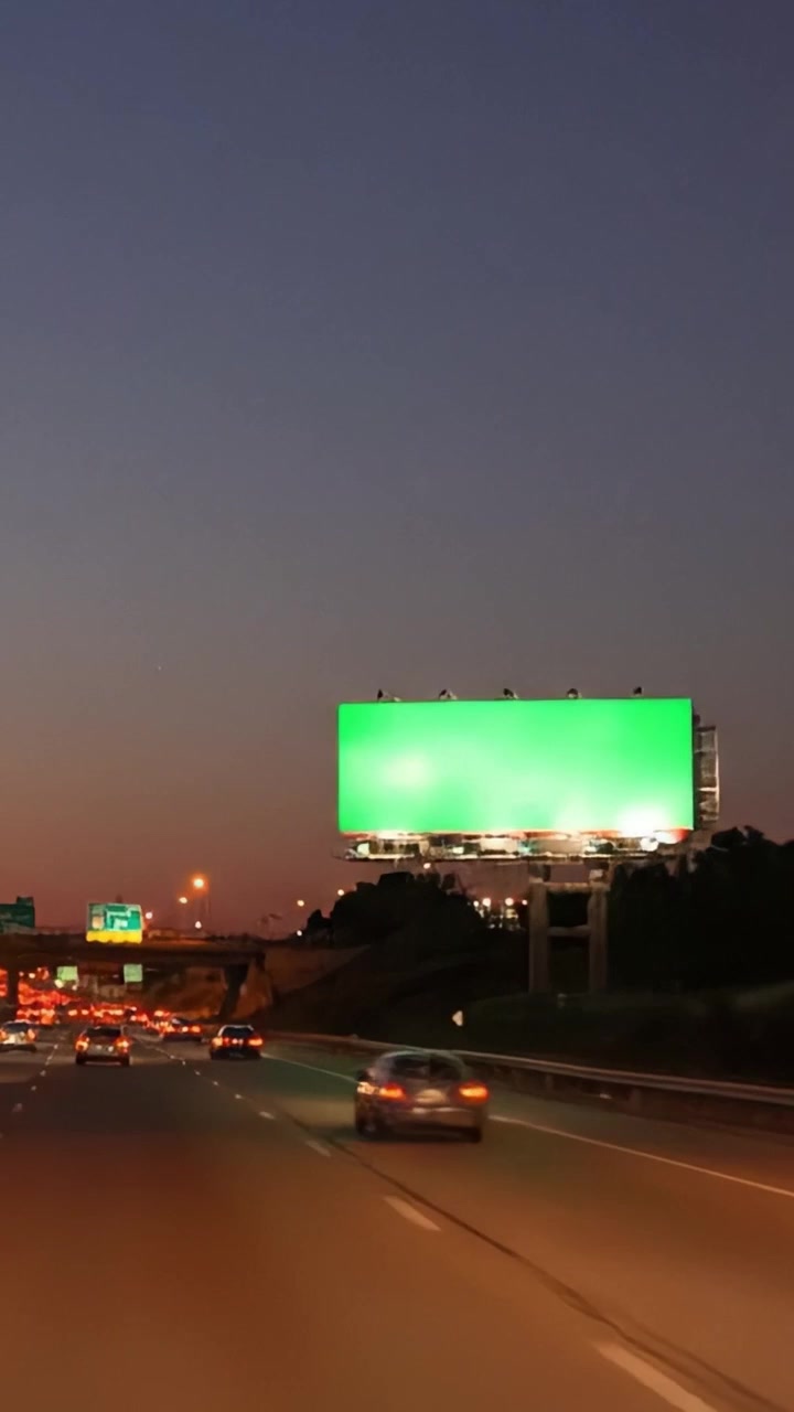 Una vibrante transición del anochecer a la noche: capturando la energía dinámica del tráfico que pasa por vallas publicitarias con colores vívidos a lo largo de la autopista.