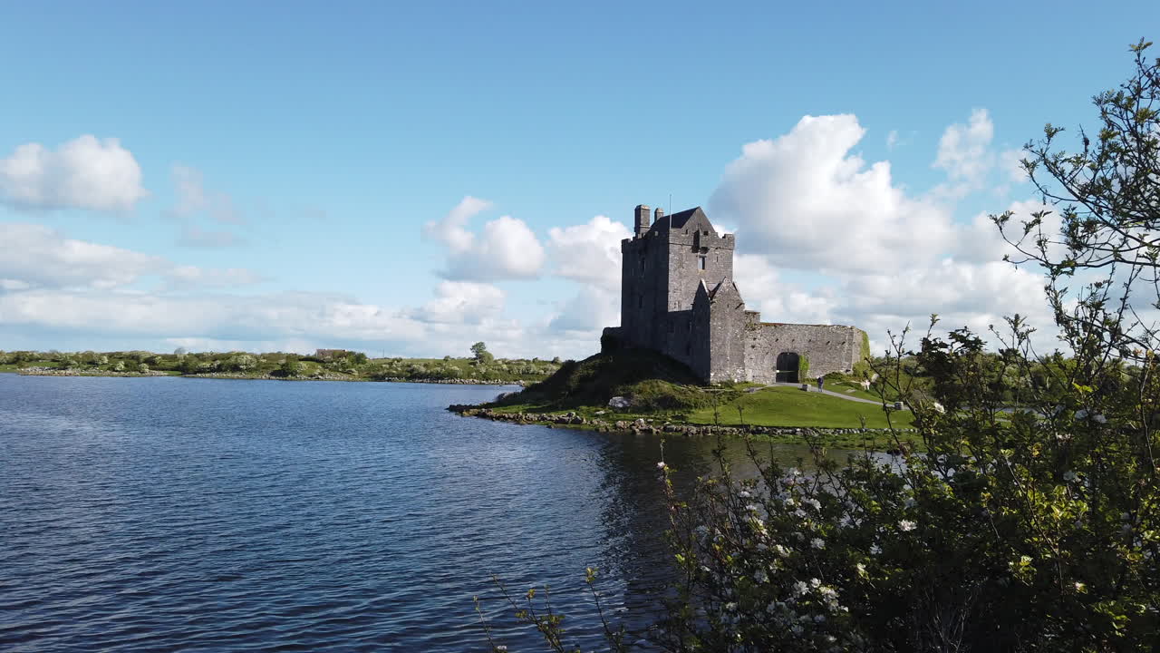 Tranquil waters reflect the historic Dunguaire castle under a bright blue sky, creating a picturesque irish landscape