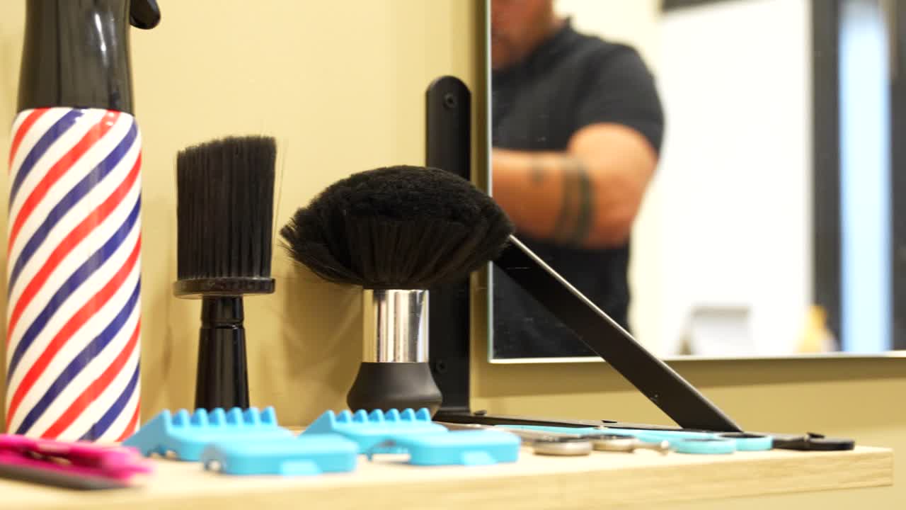 Panning left view of barber desk with tools and hairdresser working visible in mirror reflection