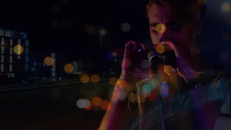 animation of blurred night road traffic over caucasian man playing harmonica on concert