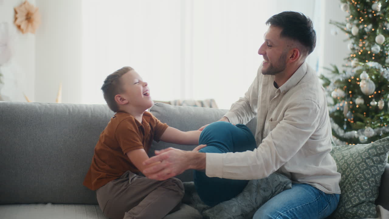 padre e hijo teniendo pelea de almohadas en el sofá regocijándose y riendo