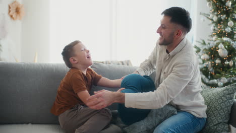 padre e hijo teniendo pelea de almohadas en el sofá regocijándose y riendo