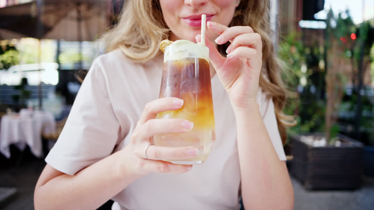 View of a woman holding and drinking a cold brew espresso shot drink with matcha foam and straw in a cafe