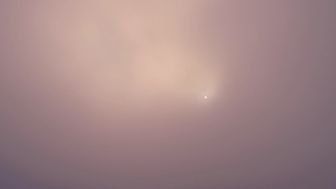 Flying up over the top of a summit with the sun behind the clouds