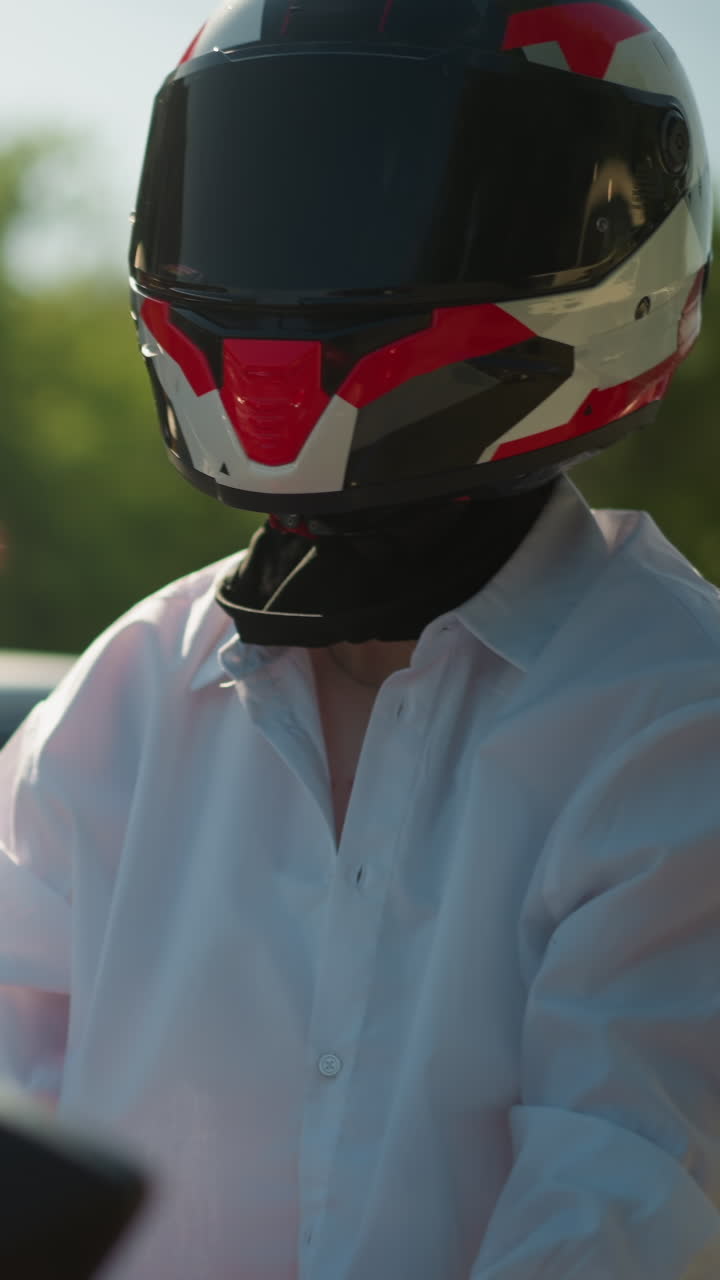 una motociclista femenina, con casco, está esperando el tráfico, inclinándose ligeramente hacia atrás, en el fondo, se ve un coche borroso con personas dentro, ralentizando debido al tráfico