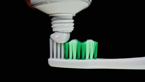 a toothbrush being loaded with some toothpaste, dark background