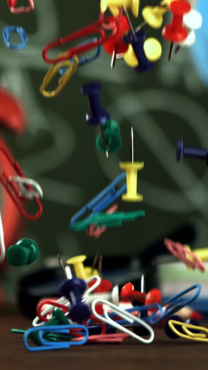 Colorful Paper Clips and Pushpins Falling onto a Desk in Slow Motion