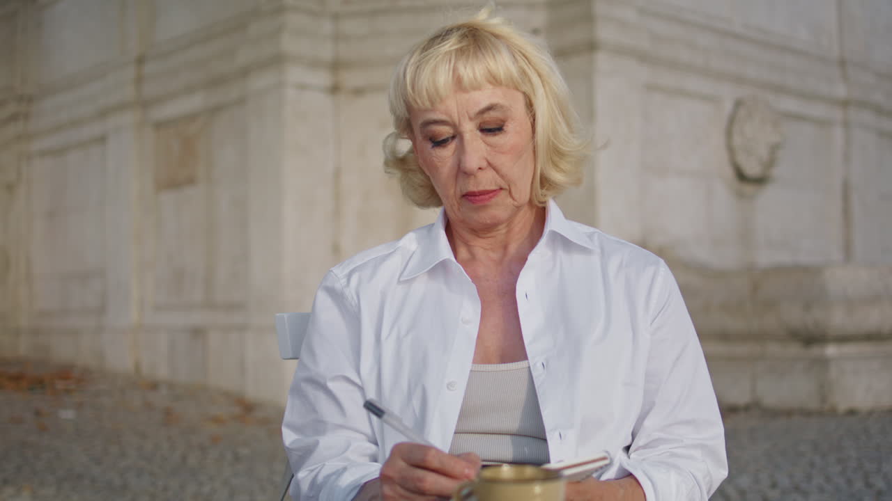 Beautiful pensioner writing diary outdoors close up. Old woman making notes
