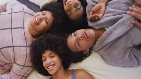 portrait of happy diverse female friends lying on bed and smiling in bedroom