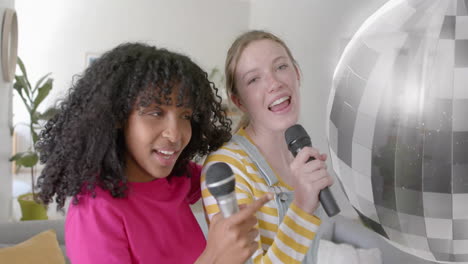 animation of mirror ball over happy diverse teenage girls with microphones singing karaoke at home