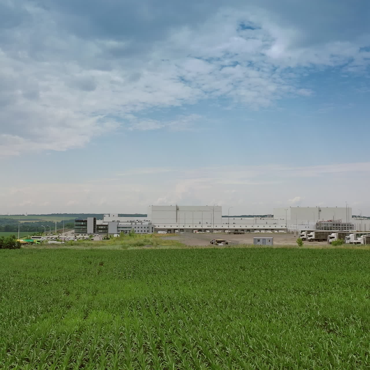 Flying over green field intoindustrial plant. Modern territory of manufacturing complex under blue sky. Camera motion forward.