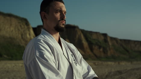 Calm-karate-man-standing-sand-close-up.-Sportsman-enjoying-beautiful-nature.