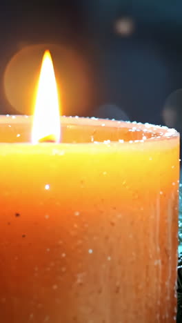 a candle is lit on a table with pine cones and snowflakes. the scene is warm and cozy, with the candle providing a soft glow that illuminates the pine cones and snowflakes