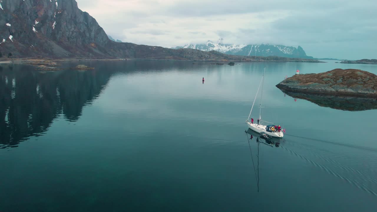 Aerial drone shot of a foggy ocean in Lofoten Norway. With rocks and mountains in the background. And a sailboat sailing in the foreground.