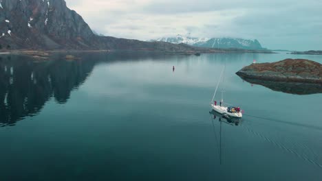 aerial drone shot of a foggy ocean in lofoten norway. with rocks and mountains in the background. and a sailboat sailing in the foreground.