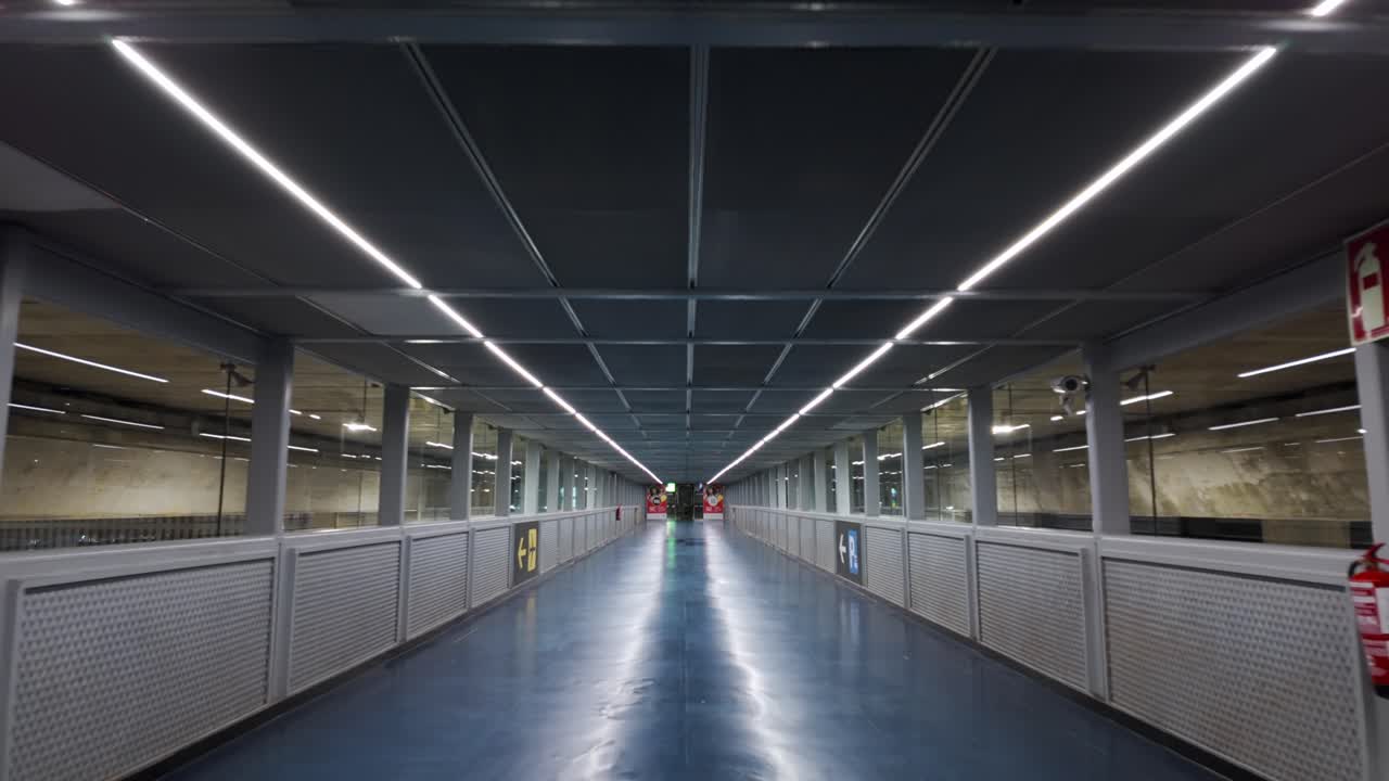 Interior view of the Alicante Airport terminal walkway featuring a blue floor and fluorescent lighting. This modern architecture and travel infrastructure is designed for efficient transportation