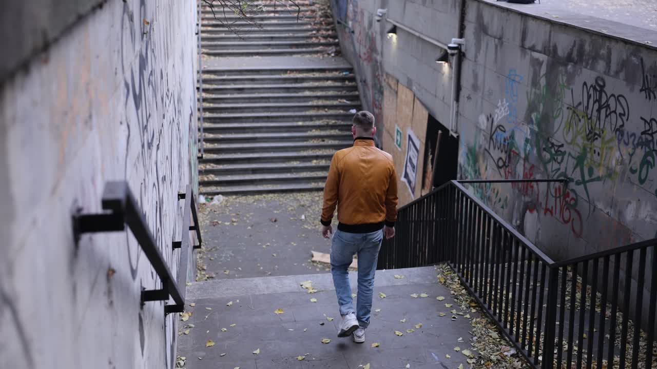 Un uomo con abiti autunnali scende i gradini di un passaggio sotterraneo.