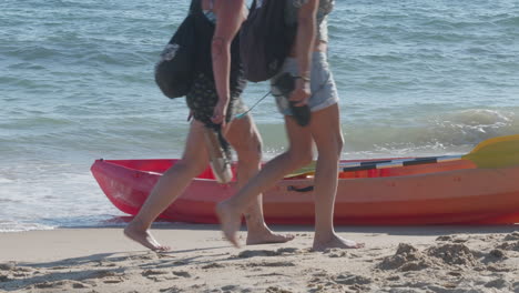 people walking on a sandy beach next to a red kayak and the ocean