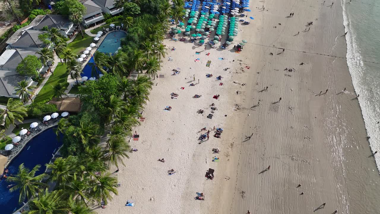 드론 영상은 활기차고 활기찬 해변과 열대 풍경을 보여주는 활기찬 푸켓 해안을 따라 활기찬 우산과 해변을 방문하는 사람들을 포착합니다.