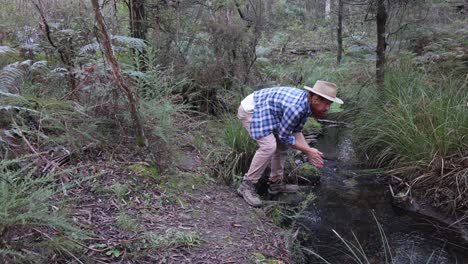 Ein-Buschmann-Mit-Akubra-Hut-Trinkt-Frisches-Wasser-Aus-Einem-Bach-Im-Australischen-Busch