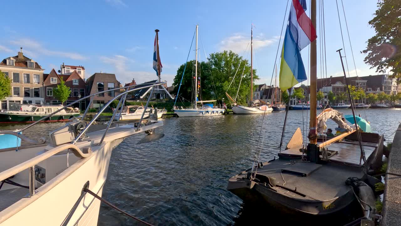 Sunny afternoon view of docked boats, canal houses, and waving flags in Haarlem marina