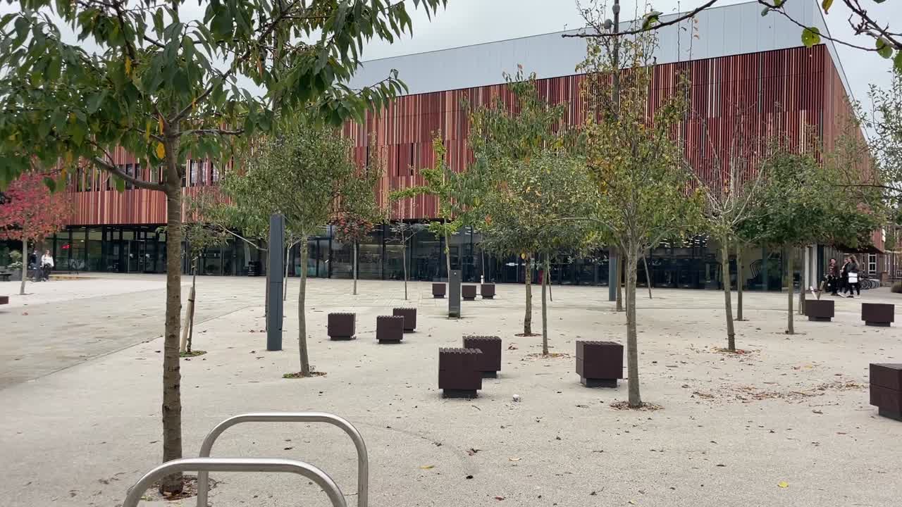 Modern park area with bike racks, benches, and trees outside Ravelin Park sports center in Portsmouth.
