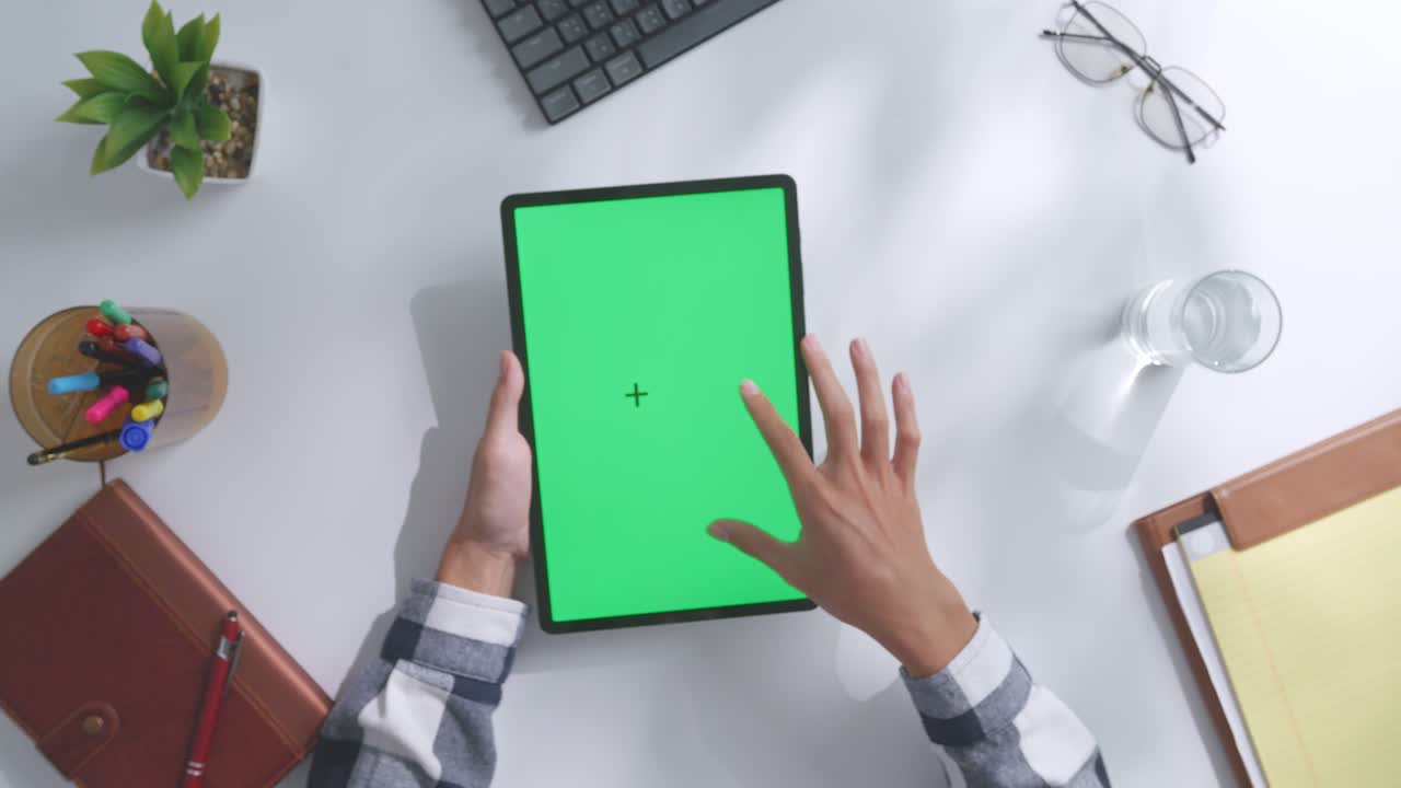 vista de arriba hacia abajo de una computadora portátil con pantalla verde simulada pantalla chromakey en un escritorio de oficina de madera al lado de la libreta con bolígrafos, gafas y un vaso de agua.