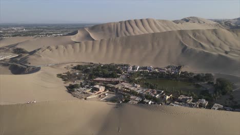 aerial orbits tourists on dune, revealing huacachina oasis far below