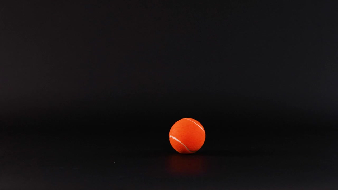 Tennis ball rolling across a dark surface