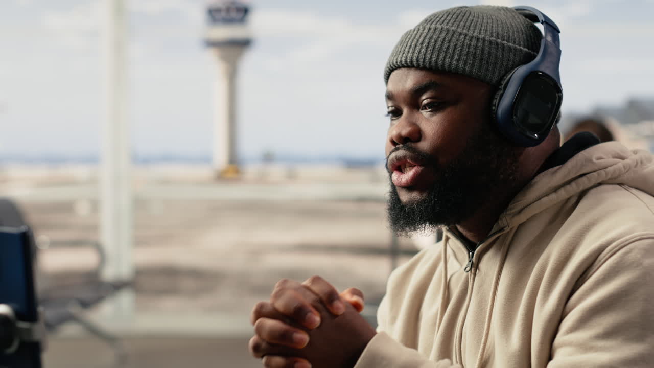 Afroamerikansk mand med hovedtelefoner taler i videoopkald i lufthavnen