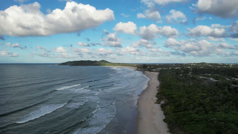 Byron bay's coastline with waves, lush greenery, and a vibrant sky, aerial view