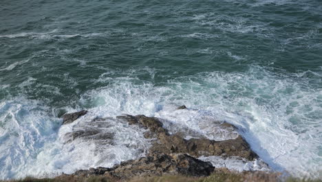 mirando hacia abajo en la cara de un acantilado a las olas rompiendo en las rocas de abajo