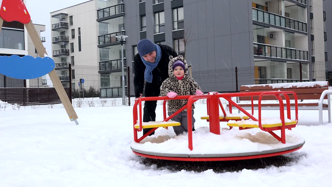 padre y la niña bebé giran en círculo en el patio de recreo al aire libre en el jardín de invierno.