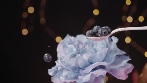 Blueberries-falling-onto-white-spoon-and-bouncing-off-blue-flower