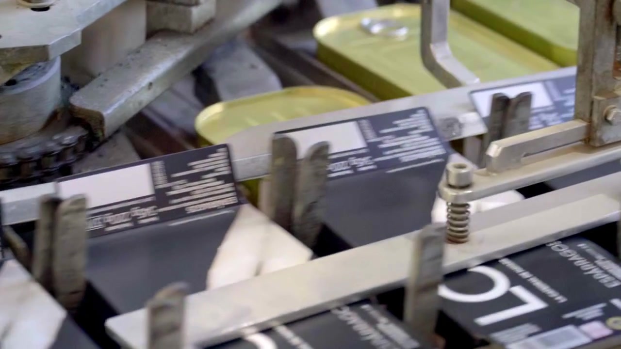 close-up of a machine labeling metallic containers, cans of asparagus, in an industrial setting, indicating the labeling process for packaged goods.
