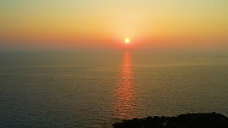 Vista-Aérea-De-La-Puesta-De-Sol-Naranja-Dorada-Sobre-El-Mar-Jónico-Con-Tiro-Hacia-Atrás-Sobre-La-Isla-De-Lefkada