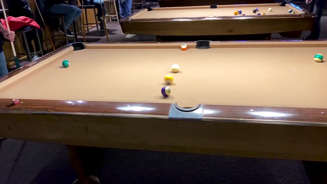 man playing pool in a dark bar, he hits the ball with a cue and hits the hole
