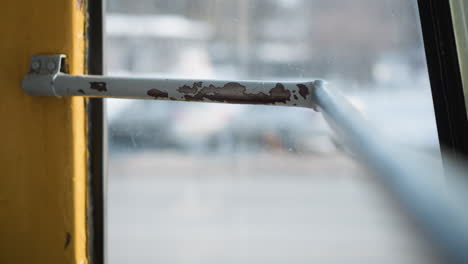 close view of door handle inside moving train, chipped paint on metal bar, winter street blurred through window, gentle vibration and light reflections convey gritty urban commute mood