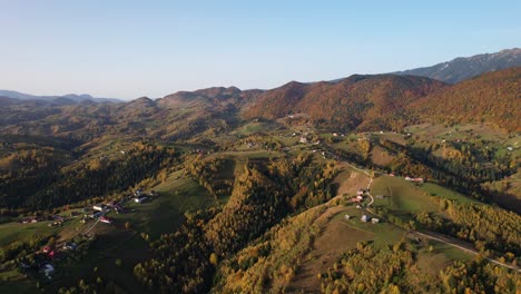 Autumn-colors-blanket-Magura-Village-with-picturesque-hills-under-a-clear-sky,-aerial-shot