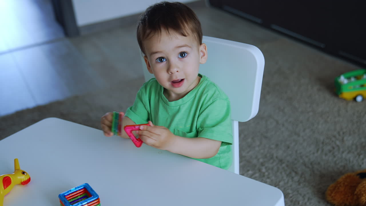Adorable toddler plays with the toys sitting at the desk. Lovely baby learning colors and shapes. Top view.