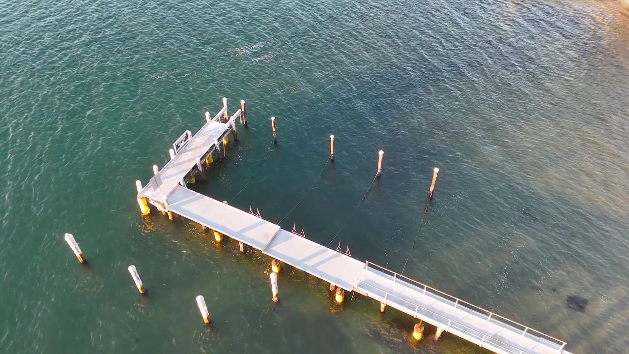 Ripresa aerea con drone di un molo di legno su acqua turchese limpida a Nelson Bay