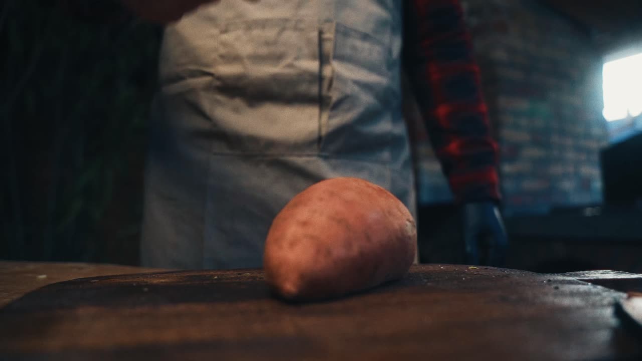 una persona en un delantal de pie detrás de una patata dulce en una tabla de cortar de madera