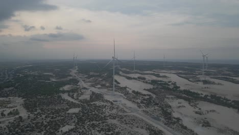 Drone-flying-toward-windmill-farm-on-white-sandy-beach-in-Quang-Binh,-Vietnam